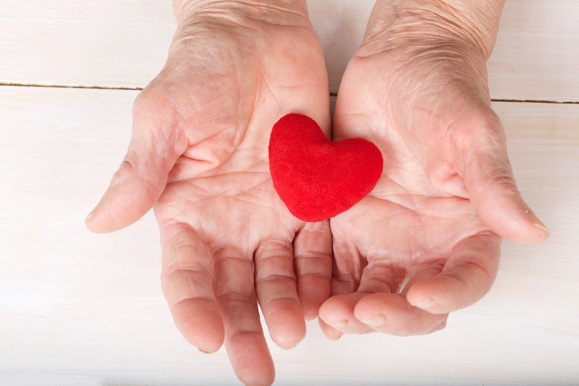 Old woman keeps a plush red heart in her palms